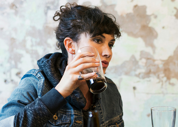 Young woman in a denim jacket drinking from a glass, reflecting on savage insults shared by 80 people.