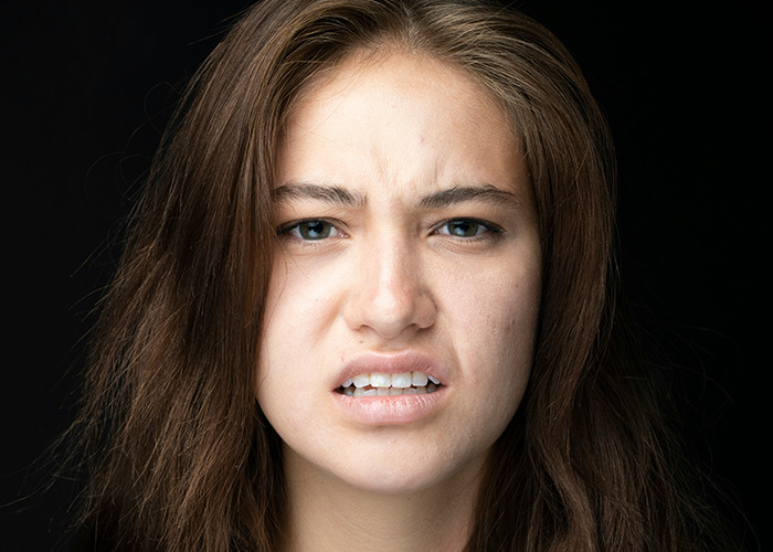 Young woman with confused expression against black background, illustrating reaction to savage insults in conversation.