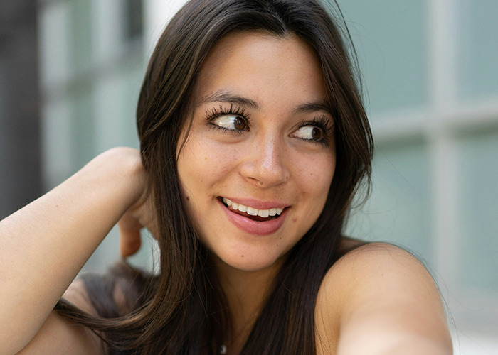 Young woman with long brown hair smiling and looking aside, illustrating reactions to savage insults shared online.