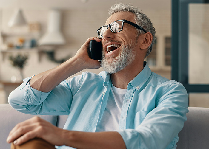 Older man with gray hair and glasses laughing while talking on a phone, representing savage insults conversation.