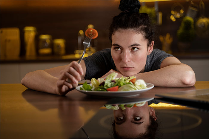 Young woman looking frustrated while holding a fork over a salad, reflecting on loved ones taking Ozempic. Young woman looking frustrated while holding a fork over a salad, reflecting on loved ones taking Ozempic.