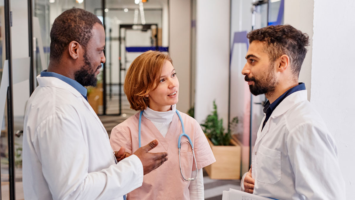 Three medical professionals in white coats and scrubs having a discussion, symbolizing company secrets and trust.