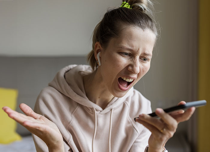 Frustrated woman in a hoodie angrily speaking on phone, expressing refusal to be a landlord for family.