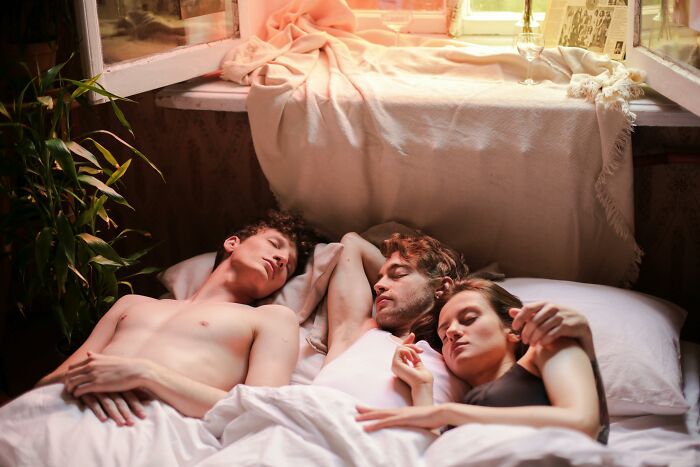 Three people lying in bed together, evoking signs that reveal a couple’s relationship troubles according to netizens.