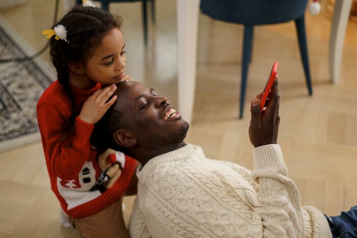 Father and daughter smiling together while looking at a phone, illustrating outrageous student names shared by a teacher.