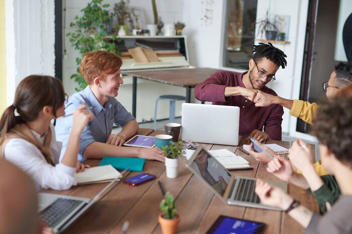 Group of young professionals collaborating around a table with laptops and coffee, emphasizing teamwork and staying hydrated.
