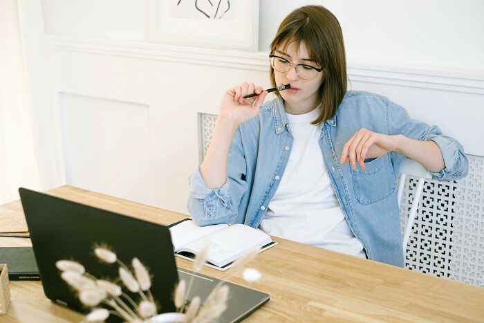 Young woman wearing glasses, thinking while solving 39 true-or-false questions on a laptop at a wooden desk. Young woman wearing glasses, thinking while solving 39 true-or-false questions on a laptop at a wooden desk.