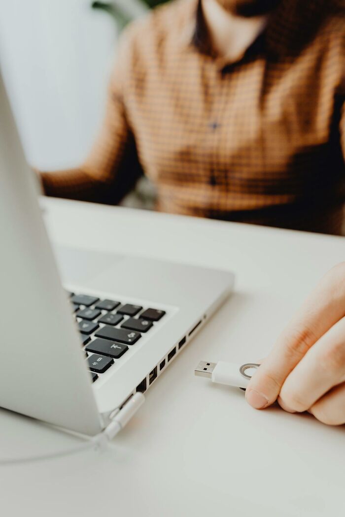 Person in a brown checkered shirt holding a USB drive near a laptop, symbolizing revenge on bosses through digital means.