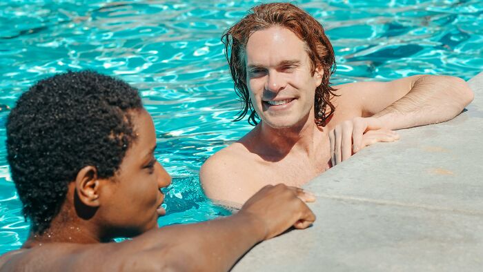 Two men in a pool, one smiling and holding the edge, illustrating unusual behaviors people did in public.