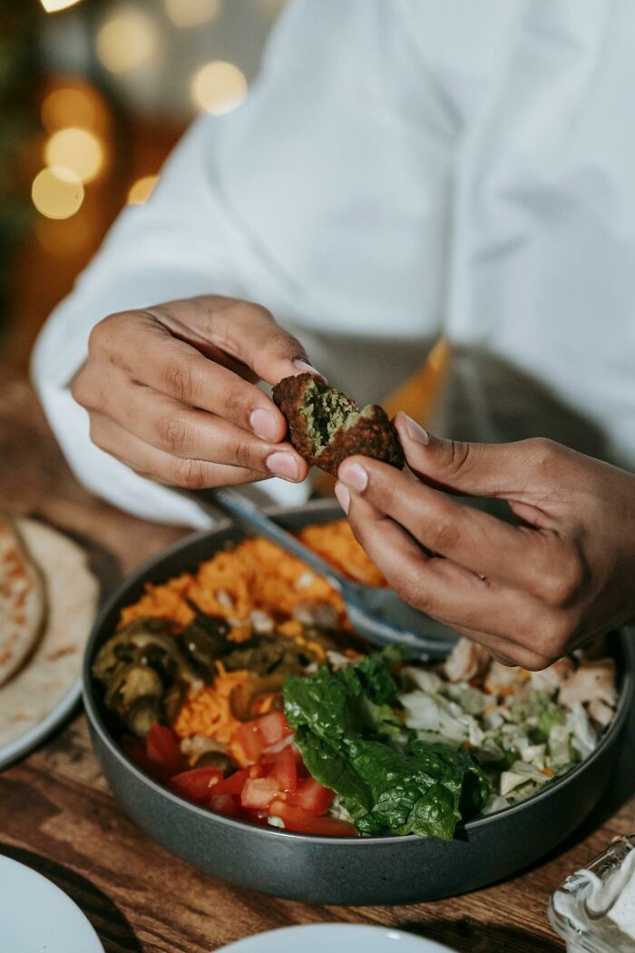 Person breaking falafel piece over a bowl of rice, vegetables, and salad, promoting healthy eating and stay hydrated habits.