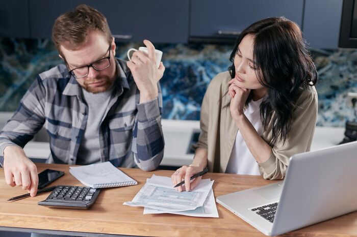 Two people discussing financial documents at a table with a laptop, calculator, and phone, focusing on staying hydrated.