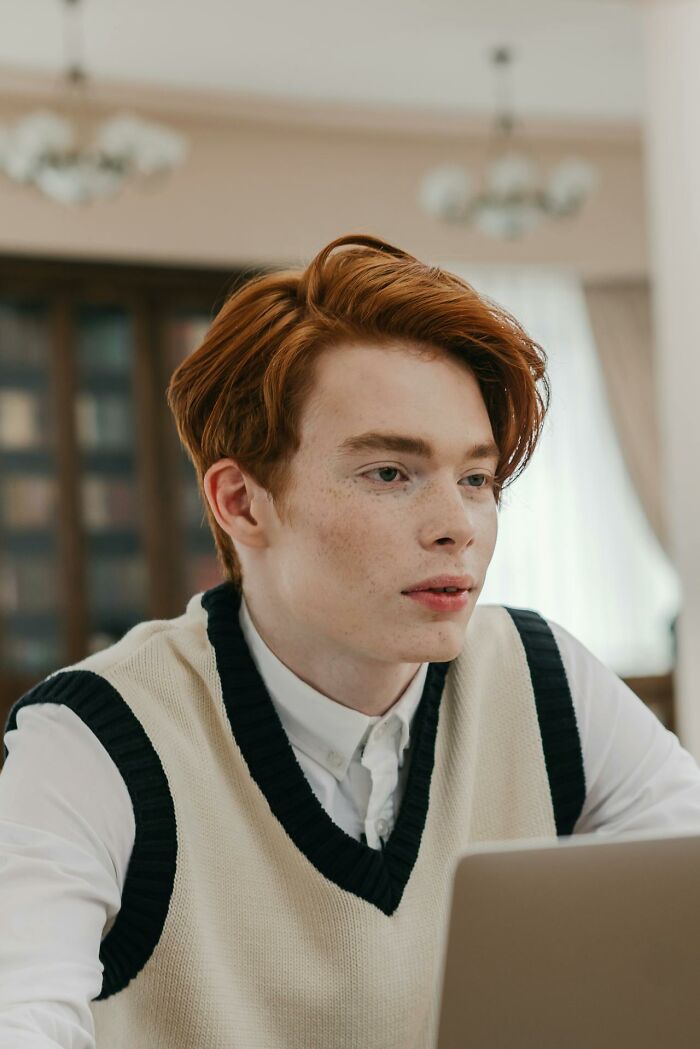 Young red-haired man working on laptop, focused in an office setting, illustrating stories of revenge on their bosses.