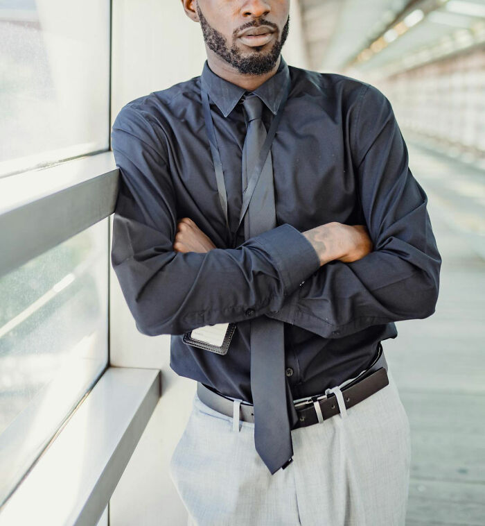 Man in black shirt and tie standing with arms crossed, reflecting on stories of revenge on their bosses.