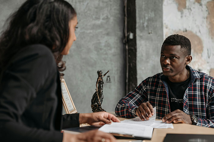 Man and woman discussing divorce papers at a desk with a Lady Justice statue between them in a legal office setting Man and woman discussing divorce papers at a desk with a Lady Justice statue between them in a legal office setting