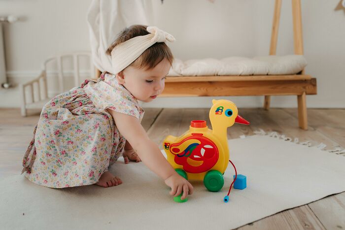 Toddler playing with colorful plastic toy duck highlighting trends leading to overconsumption concerns in modern families.