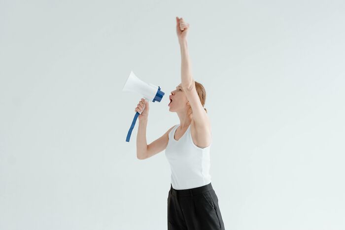 Woman in white tank top shouting through a megaphone raising her fist, illustrating country stereotypes concept. Woman in white tank top shouting through a megaphone raising her fist, illustrating country stereotypes concept.