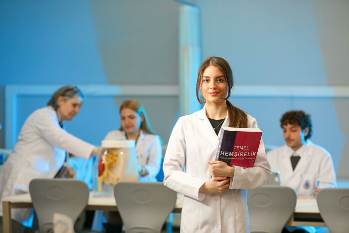 Young female scientist holding a book in a lab with colleagues studying anatomy models, illustrating use of bodies donated for science.