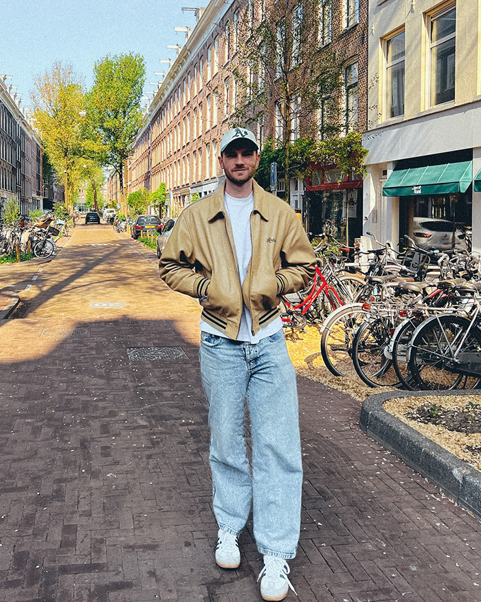 Man wearing a tan jacket and cap walking on a sunny street with bicycles parked, illustrating passenger allergy request debate context. Man wearing a tan jacket and cap walking on a sunny street with bicycles parked, illustrating passenger allergy request debate context.