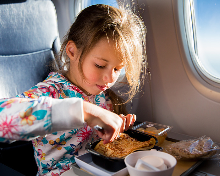 Child eating a meal on a flight near a window, illustrating passenger allergy request during air travel debate. Child eating a meal on a flight near a window, illustrating passenger allergy request during air travel debate.