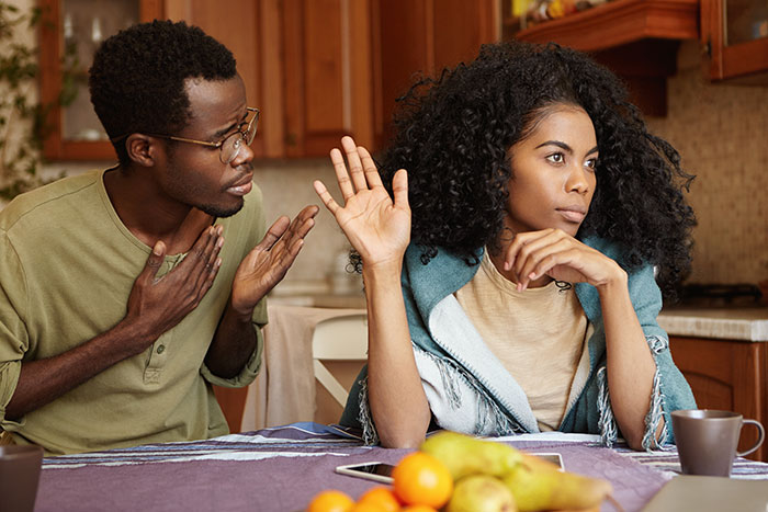 Man refuses to give home to sister and her family, woman raising hand in disagreement during a kitchen conversation.