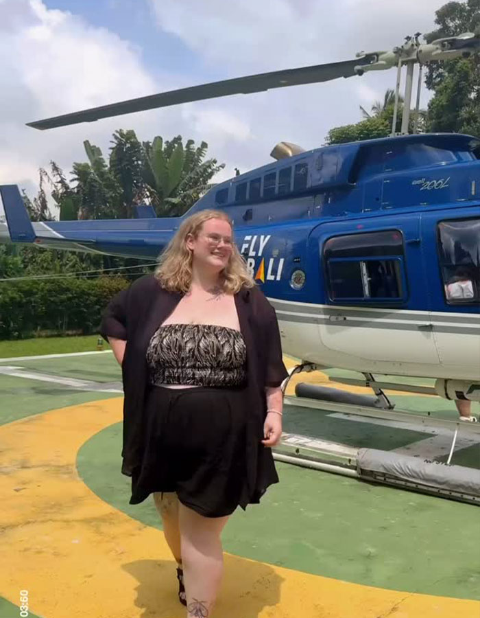 Plus-size traveler smiling outdoors near a blue helicopter, illustrating plus-size traveler experiences in aviation travel. Plus-size traveler smiling outdoors near a blue helicopter, illustrating plus-size traveler experiences in aviation travel.
