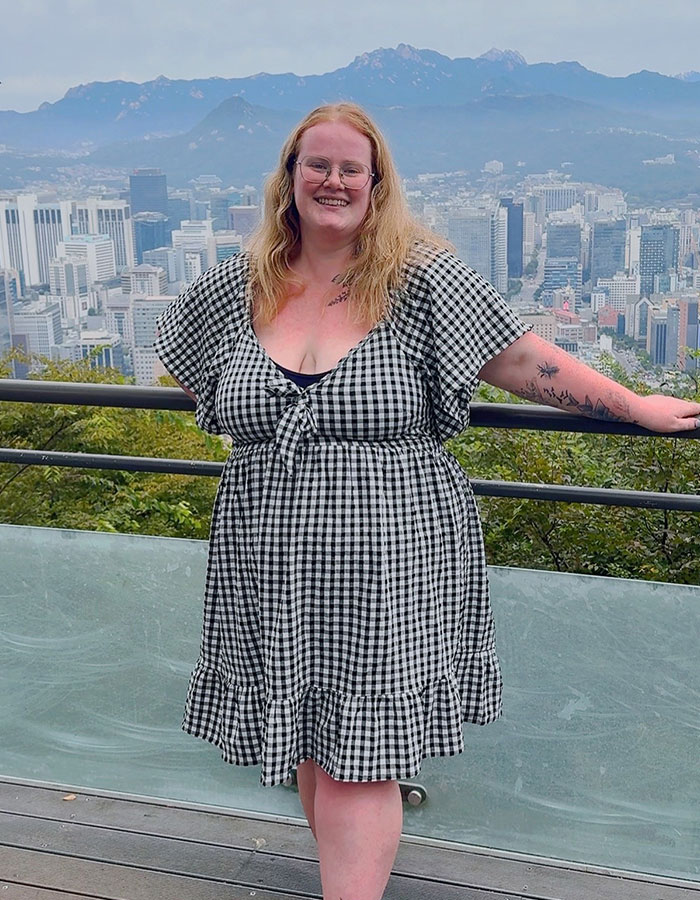 Plus-size traveler smiling outdoors with cityscape backdrop, sharing why she won’t book two airline seats Plus-size traveler smiling outdoors with cityscape backdrop, sharing why she won’t book two airline seats