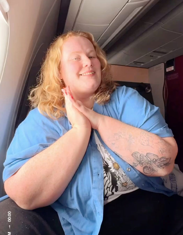 Plus-size traveler smiling on airplane, sharing reasons for not booking two airline seats, facing criticism. Plus-size traveler smiling on airplane, sharing reasons for not booking two airline seats, facing criticism.