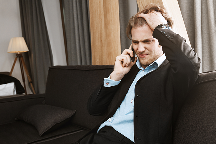 Gay man in suit sitting on couch, looking distressed during phone call about wedding invitation misunderstanding. Gay man in suit sitting on couch, looking distressed during phone call about wedding invitation misunderstanding.