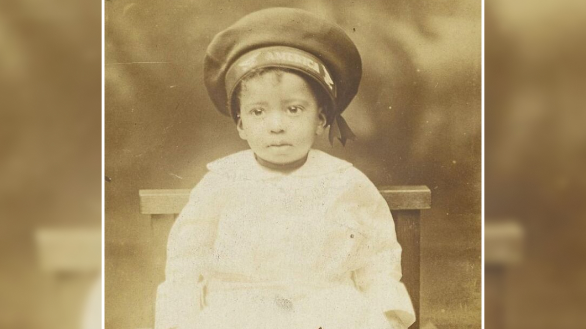 Vintage postcard featuring a young child in 1930s attire wearing a large sailor hat, sepia tone photograph.