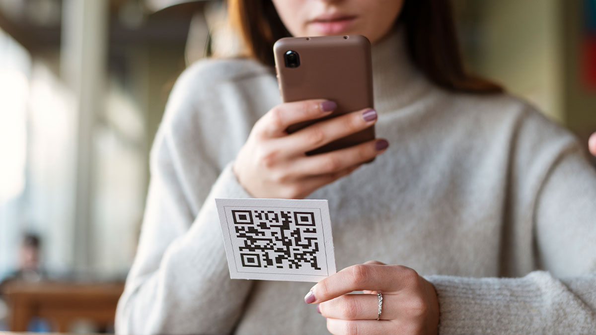 Woman scanning QR code on wedding invite to send money using smartphone in a cozy indoor setting