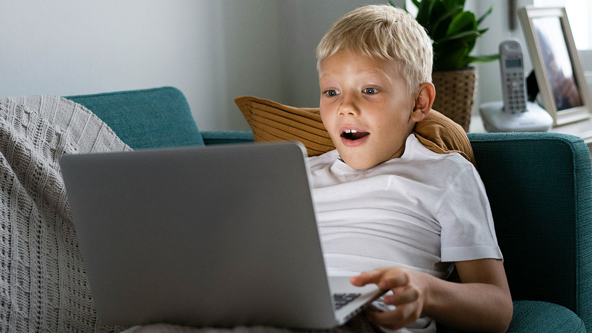 Young boy with autism sitting on couch looking surprised at laptop screen indoors at home setting