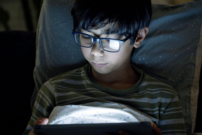 Young boy with glasses using a tablet in dim light, representing concerns around autistic child safety issues. Young boy with glasses using a tablet in dim light, representing concerns around autistic child safety issues.