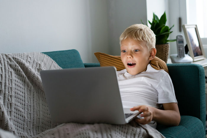 Young boy likely with autism using a laptop on a couch, highlighting concerns about child safety in family settings.