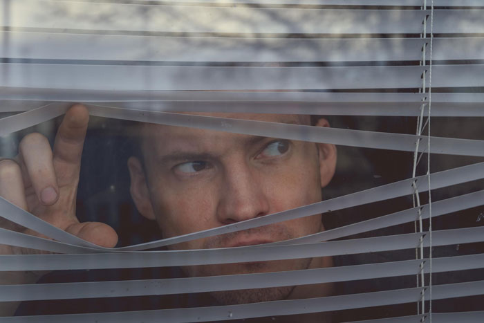 Man peeking through window blinds suspiciously, reflecting someone considering public road as personal parking space situation. Man peeking through window blinds suspiciously, reflecting someone considering public road as personal parking space situation.