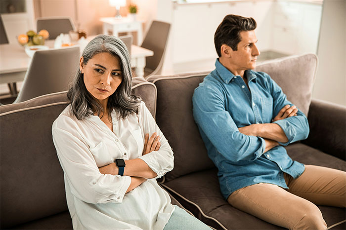 Woman with PhD looks upset sitting opposite her husband on couch with arms crossed in bright modern living room. Woman with PhD looks upset sitting opposite her husband on couch with arms crossed in bright modern living room.