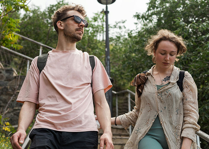 Couple walking outdoors with backpacks, highlighting controversy over tour company and bad reviews for childfree visitors.