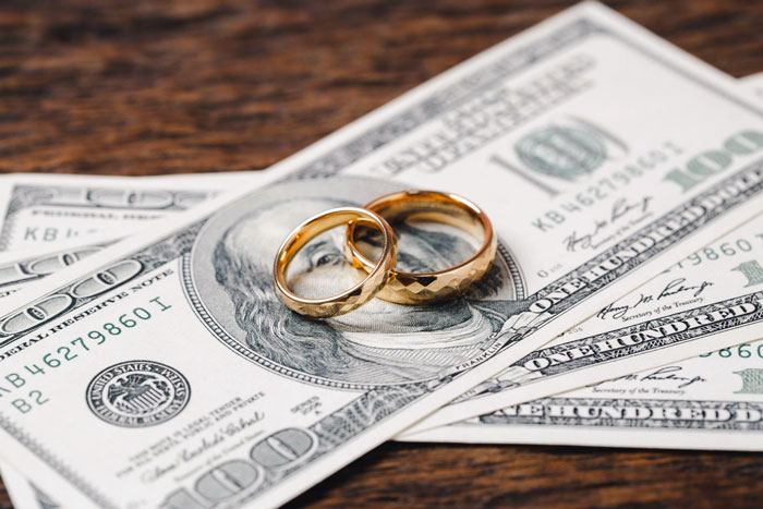 Two gold wedding rings placed on top of hundred-dollar bills representing groom discount and money issues in wedding events. Two gold wedding rings placed on top of hundred-dollar bills representing groom discount and money issues in wedding events.