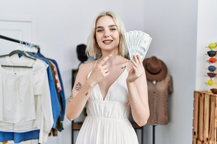 Woman in white dress holding cash and smiling inside a clothing store, illustrating groom discount and lending refusal story. Woman in white dress holding cash and smiling inside a clothing store, illustrating groom discount and lending refusal story.