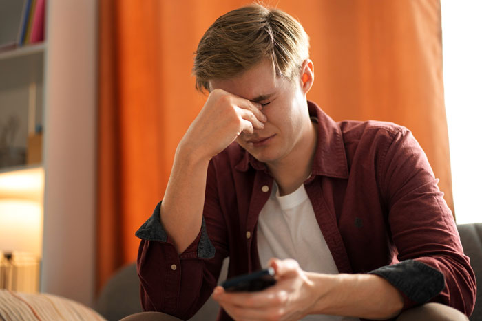 Young man looking stressed and upset, holding a phone, representing groom discount and family conflict over money. Young man looking stressed and upset, holding a phone, representing groom discount and family conflict over money.