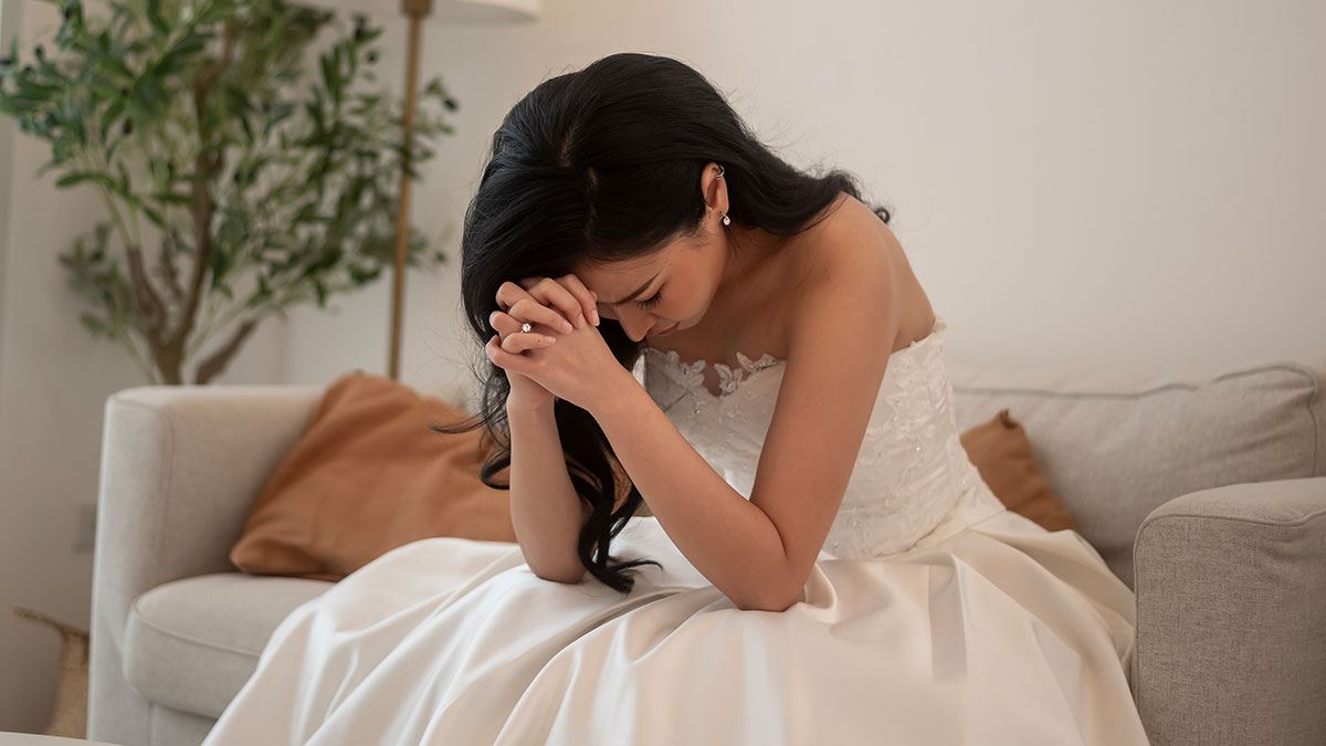 Bride in wedding dress sitting on couch, distressed and thoughtful amid family conflict involving autistic nephew.