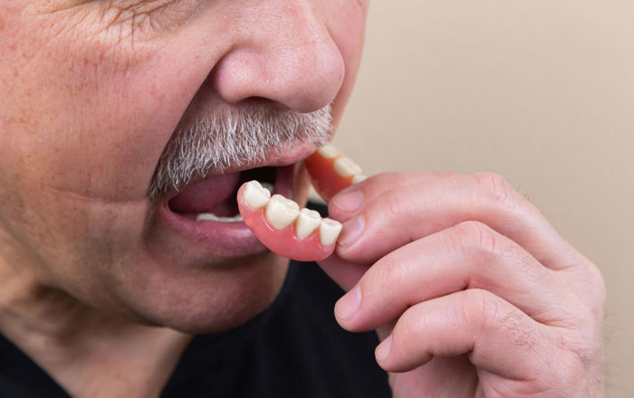 Close-up of man holding dentures, highlighting breakthrough in tooth regrowth that may replace dentures and implants. Close-up of man holding dentures, highlighting breakthrough in tooth regrowth that may replace dentures and implants.