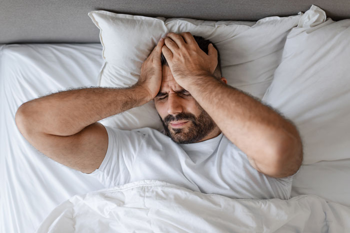 Man in bed covering ears in frustration, disturbed by loud noise at night from smart air con turned into ice machine. Man in bed covering ears in frustration, disturbed by loud noise at night from smart air con turned into ice machine.