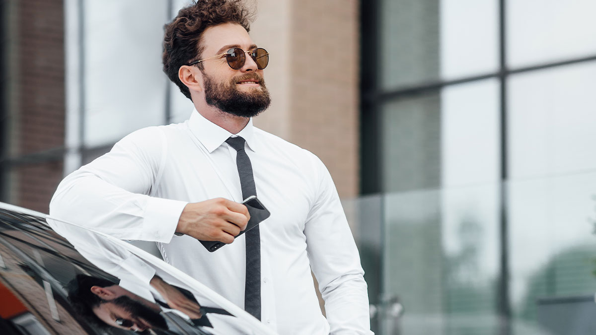 Confident man in sunglasses leaning on a car, representing unexpected things people learned about the rich.