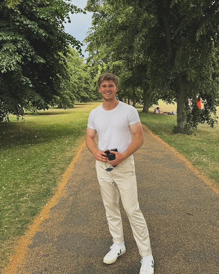 Robert Irwin smiling on a park pathway wearing a white shirt, light pants, holding sunglasses and a camera outdoors. Robert Irwin smiling on a park pathway wearing a white shirt, light pants, holding sunglasses and a camera outdoors.
