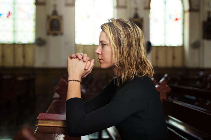Woman in black shirt sitting in church pew, deep in thought, representing disbelief in dinosaurs topic. Woman in black shirt sitting in church pew, deep in thought, representing disbelief in dinosaurs topic.