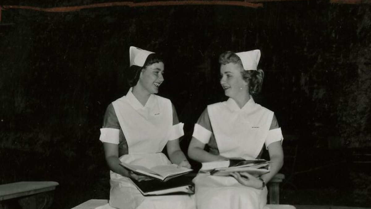 Two vintage nurses in classic uniforms smiling and holding books, embodying healing and hope.
