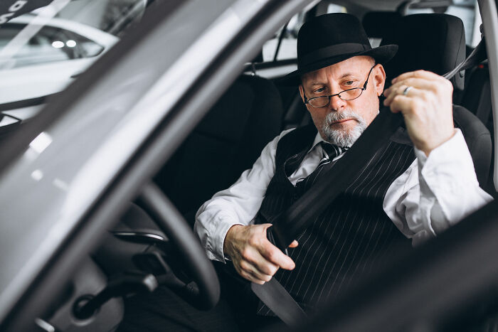 Older man in a suit and hat fastening seatbelt inside a car, illustrating McDonald's employees bizarre experiences.