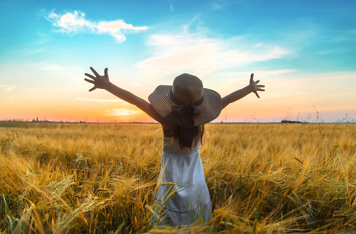 Person with sunhat standing in a golden field at sunset with arms outstretched, symbolizing life-changing moments.