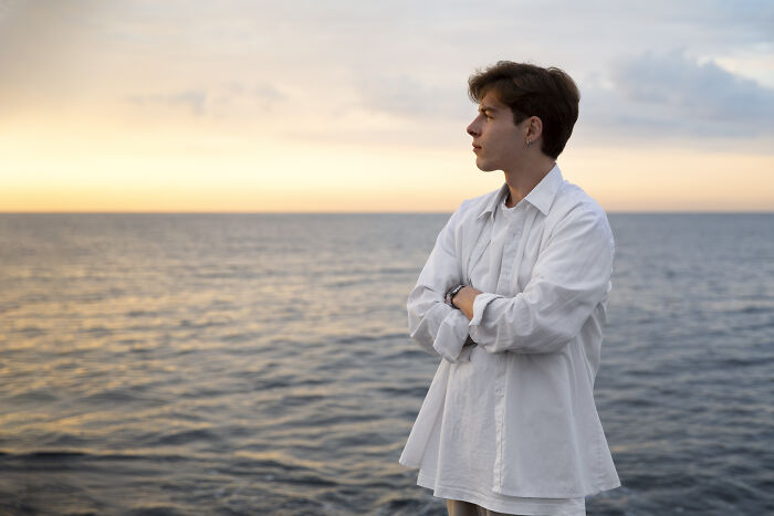 Young man in white shirt looking thoughtfully at the sea during sunset, reflecting on sentences that changed lives.