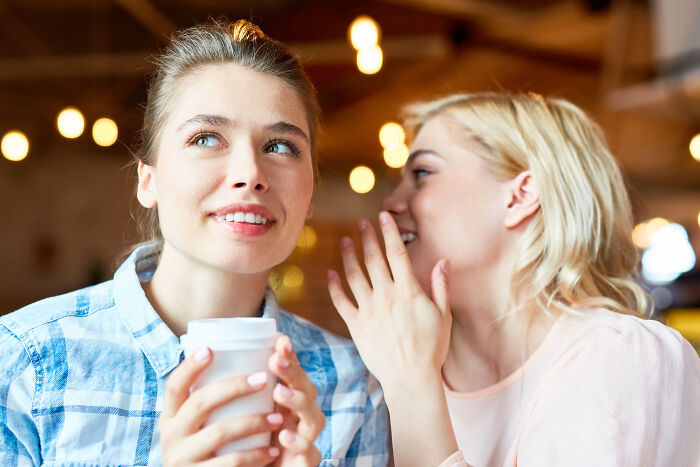 Two women in a cozy cafe, one whispering and the other smiling, sharing life-changing sentences.